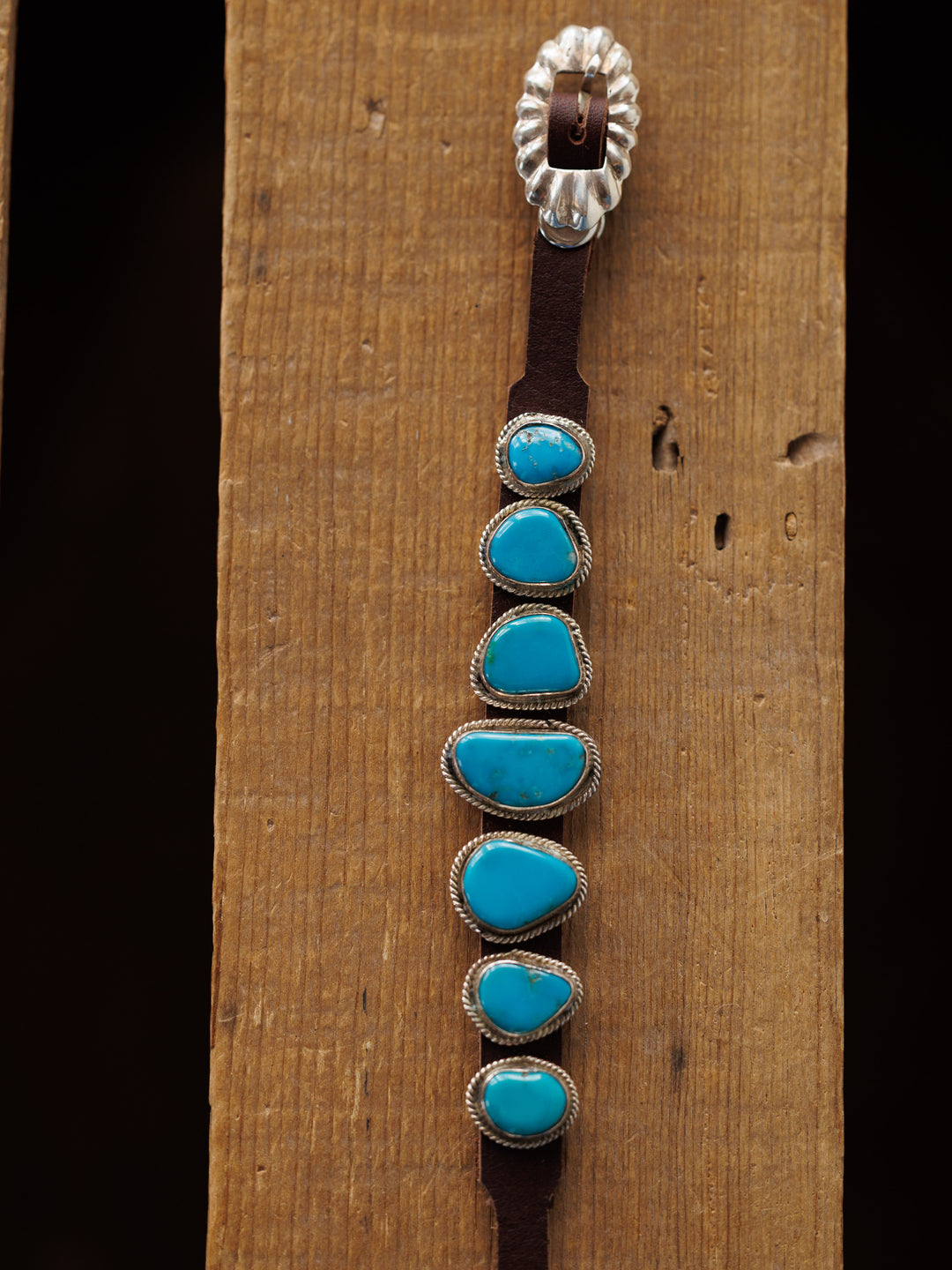 The Aguila Bracelet by Savannah Sevens western life{&}style features six genuine turquoise stones set in sterling silver on leather, displayed on a wooden surface.
