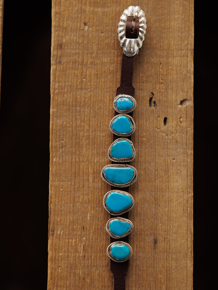The Aguila Bracelet by Savannah Sevens western life{&}style features six genuine turquoise stones set in sterling silver on leather, displayed on a wooden surface.