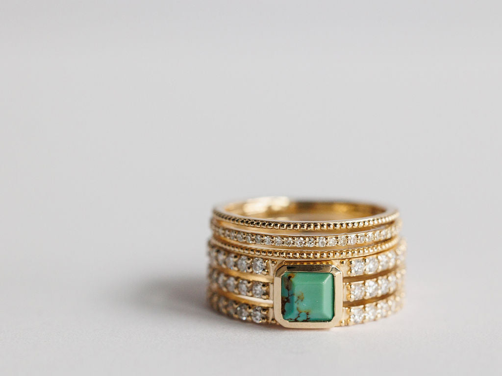 The Diamond Turquoise Ring by Savannah Sevens western life{&}style features four gold bands—three with lab grown diamonds and one showcasing a square marbled green turquoise—displayed on a plain, light background. Collaboration the Devereaux Gold.