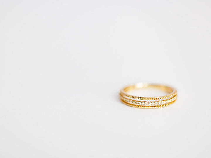 The Diamond Milgrain Ring by Savannah Sevens western life{&}style, crafted in 14K gold with intricate milgrain detailing, sits on a plain white surface, positioned to the right with empty space on the left.