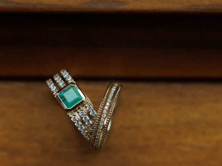 The Diamond Milgrain Ring by Savannah Sevens western life{&}style features 14K gold, multiple bands with milgrain detailing, sparkling diamonds, and a green square gemstone, beautifully displayed on a wooden surface. Collaboration the Devereaux Gold.