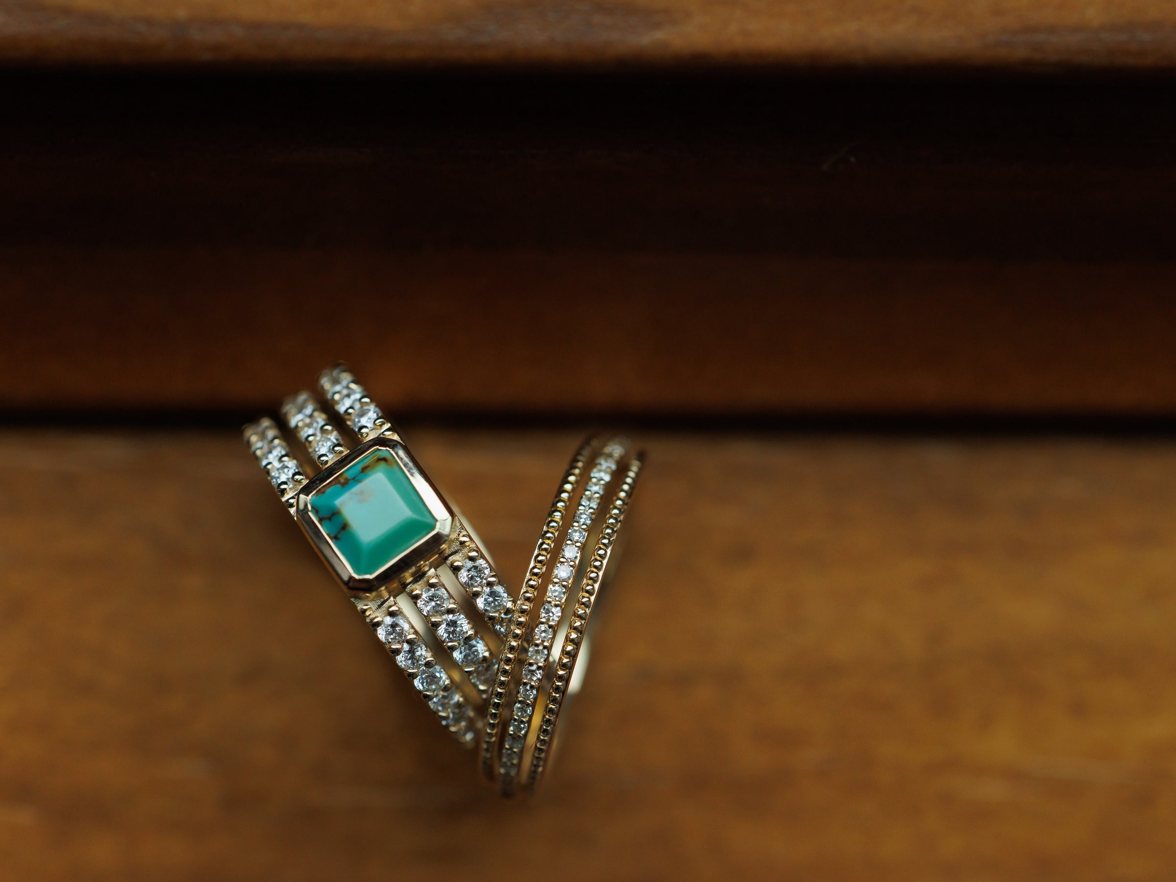 A gold ring featuring a square green gemstone and multiple bands adorned with sparkling clear stones, set against a rustic wooden background.