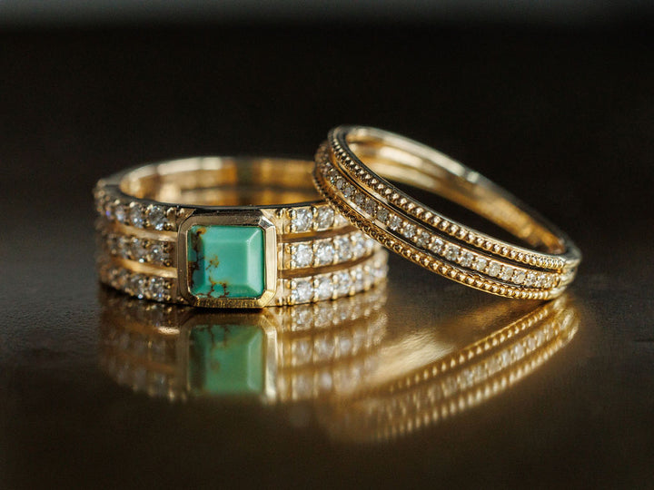 Two gold rings rest side by side: a 14K gold diamond ring with a square turquoise gemstone and Savannah Sevens western life{&}style’s Diamond Milgrain Ring, known for its fine beaded detailing and diamonds. Both are reflected on a glossy surface.