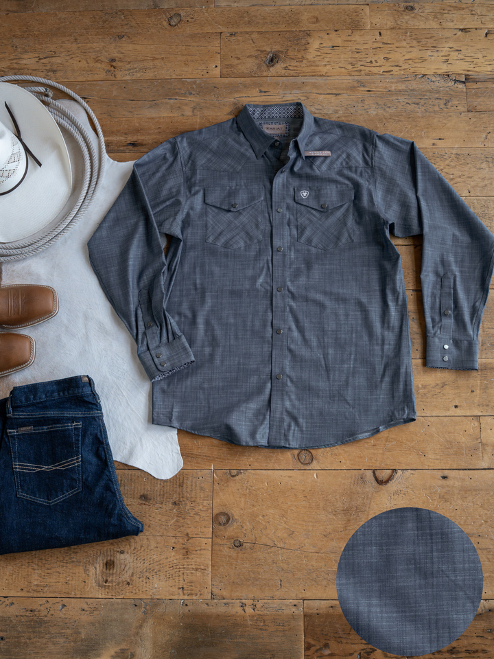 The Elkport Men's shirt by Savannah Sevens western life&style is shown flat on a wooden floor with blue jeans, brown boots, a white hat, and a cowhide rug. A close-up circle highlights the shirt’s fabric texture.
