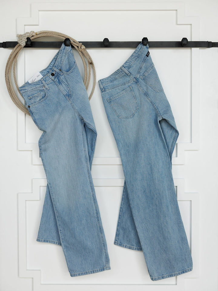 Two pairs of The Landry High Rise Slim Wide Leg Jean by Savannah Sevens western life{&}style in light blue pinstripe denim hang side by side on a black rod against a white wall, with a coiled rope looped near the left pair.