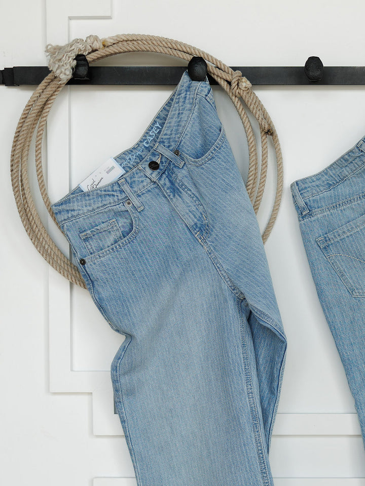 A pair of light blue Savannah Sevens western life{&}style The Landry High Rise Slim Wide Leg Jeans hangs on a black rod with a thick beige rope in the belt loop. Another high rise wide leg jean is partially visible on the right.