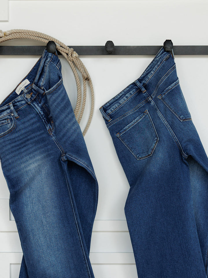 Two pairs of Savannah Sevens western life{&}style The Bristol High Rise 90's Wide Leg Jean hang by their belt loops on black hooks, with a coiled rope over one hook, set against a white wall.