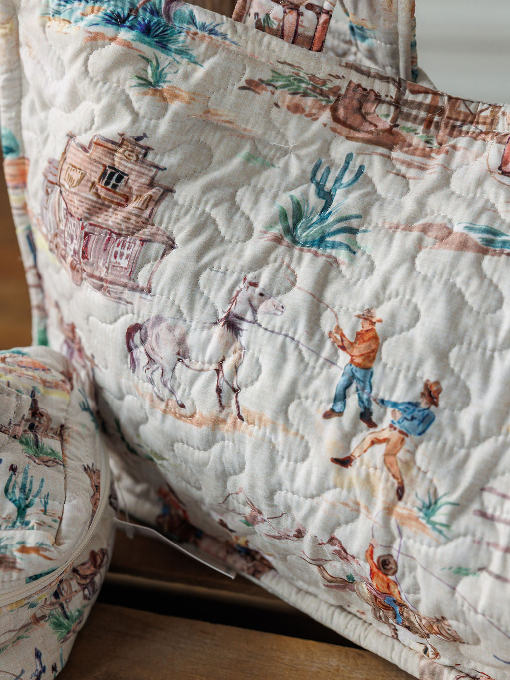 The Retro Cowboy Collection by Savannah Sevens western life & style features a handmade quilted bag with soft, muted Western prints—cowboys, horse, saloon, cacti, and desert scenery.