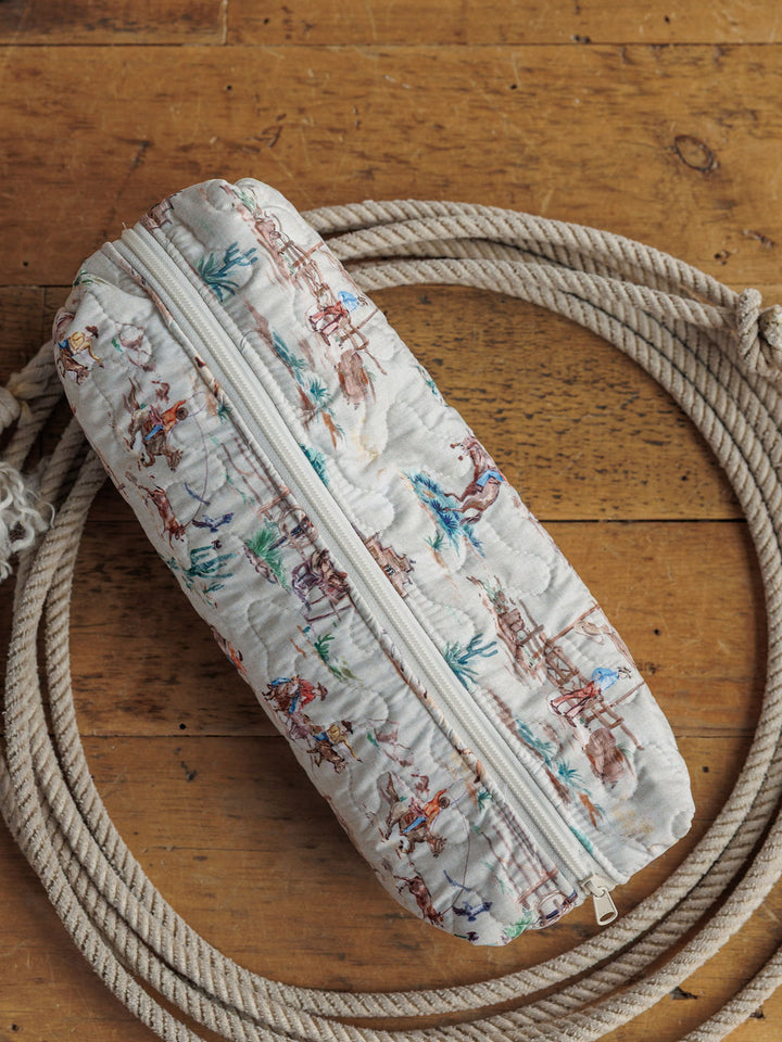 The Retro Cowboy Collection zippered fabric pouch by Savannah Sevens western life & style rests on a coiled rope atop wood, featuring cowboy, horse, and cactus illustrations.