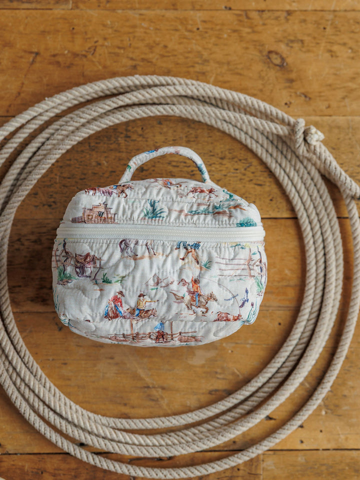 A small, handmade quilted bag with colorful illustrations and a handle from the Retro Cowboy {Collection} by Savannah Sevens western life{&}style sits coiled on a wooden floor—perfect for your western travels.