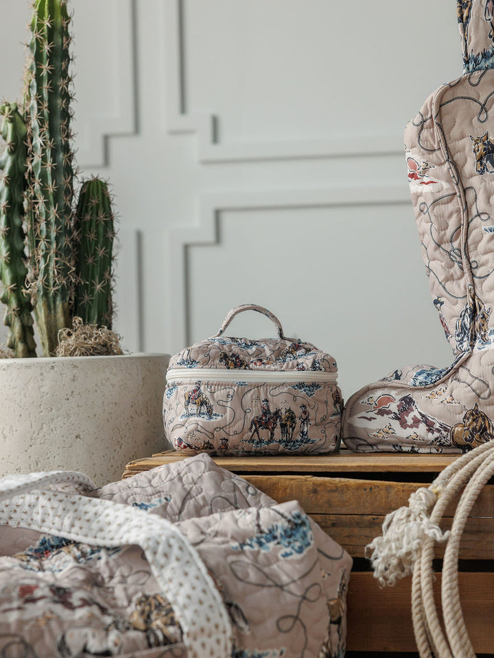 Soft quilted bags and a small box with whimsical prints from the Montana Summer Collection by Savannah Sevens western life&style are arranged on wood beside a tall cactus, set against a textured white wall.