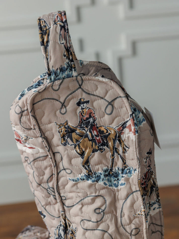 The Montana Summer quilt bag by Savannah Sevens western life{&}style features a cowboy and horse pattern on light beige with blue and brown accents. Shown from the side, the bag includes a top handle and is part of our western collection.