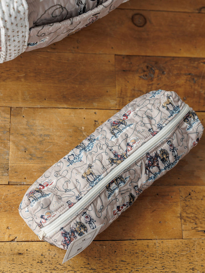 A quilted, cylindrical bag with a zipper from the Montana Summer Collection by Savannah Sevens western lifestyle rests on a wooden floor. Another matching item from the set is partially visible in the top left corner.