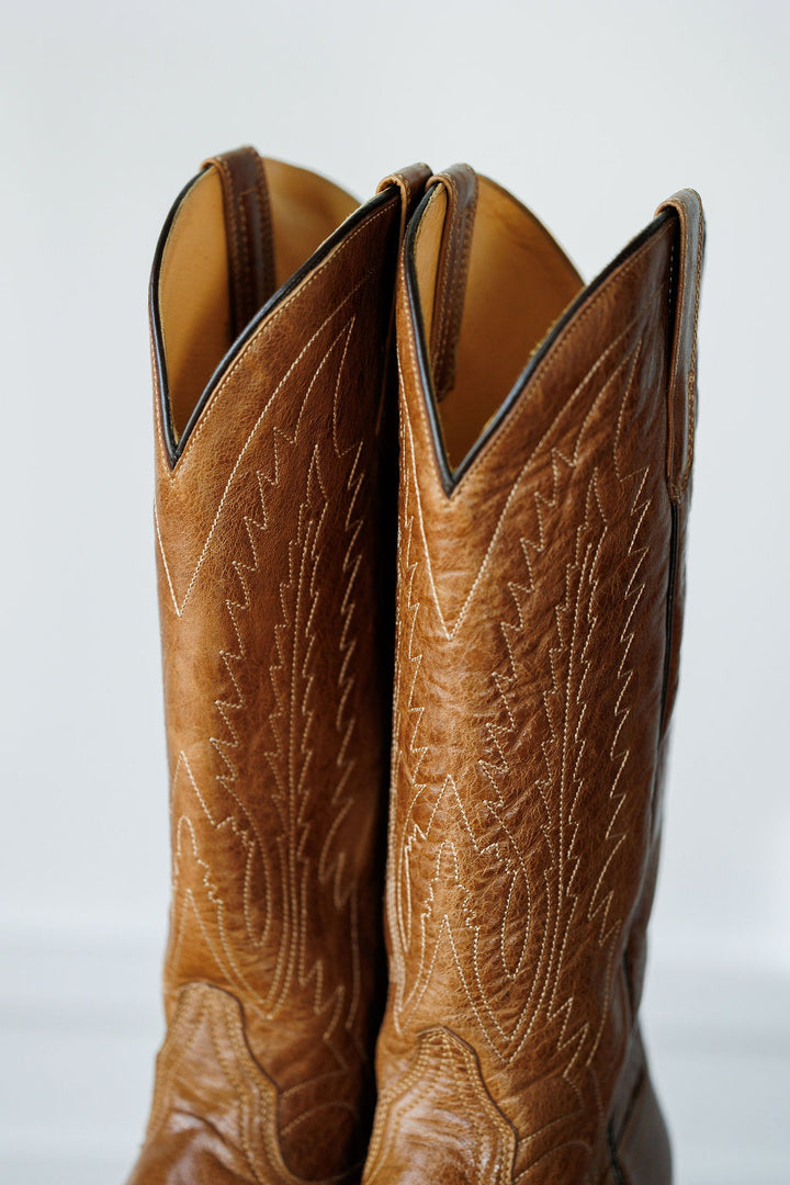 A close-up of The Balcones boots by Savannah Sevens western life{&}style, crafted from pecan leather with detailed stitching and tall, pointed tops—showcasing signature style against a plain backdrop.