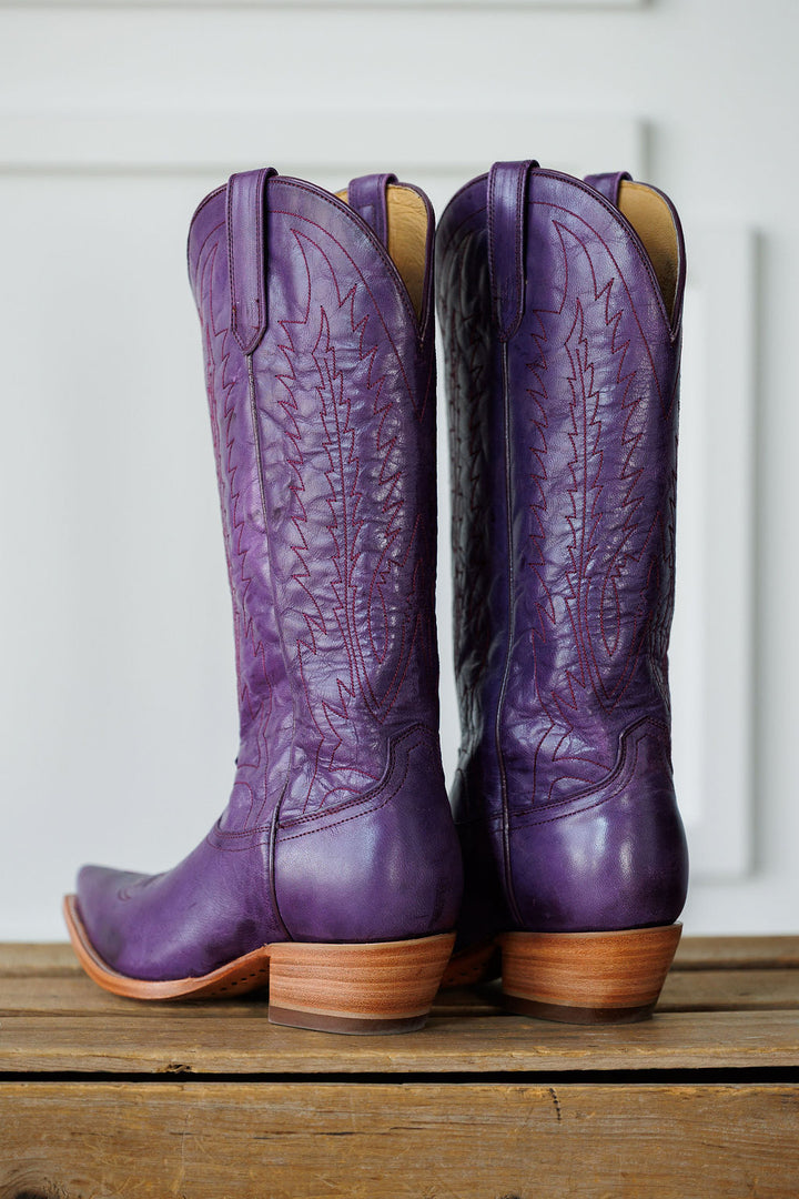 The Maricopa by Savannah Sevens western life{&}style: tall plum leather snip toe western boots with decorative stitching and light brown wooden heels, showcased on a wooden surface against a white background. Made by Black Star. 