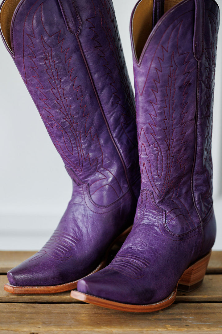 A close-up of The Maricopa plum leather snip toe western boots by Savannah Sevens western life{&}style, featuring decorative stitching and resting on a wooden surface. Made by Black Star. 