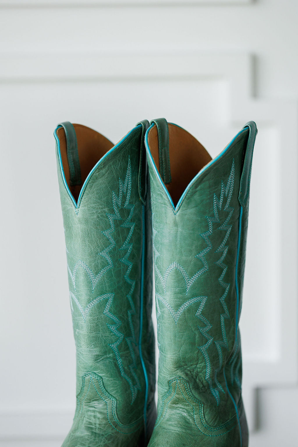 A close-up of The Carico, tall green turquoise leather western boots by Savannah Sevens western life{&}style, featuring decorative stitching and pull straps, set against a white background.