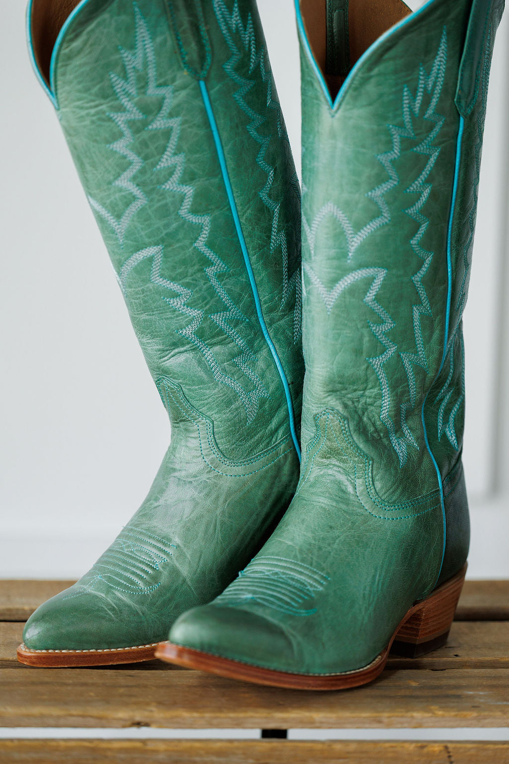 The Carico by Savannah Sevens western life{&}style: tall green turquoise leather western boots with decorative stitching and blue piping, shown on a wooden surface. Made by Black Star. 