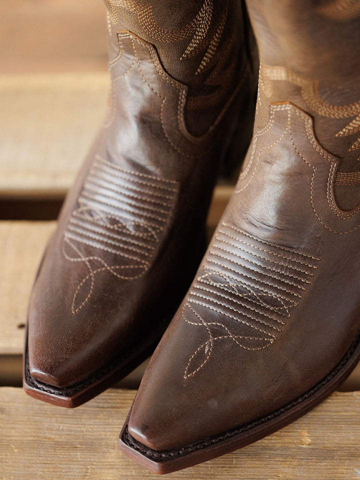 Close-up of the pointed toes on The Annie Boot {Cafe} by Savannah Sevens western life{&}style, crafted from premium goat leather with decorative stitching, displayed on a wooden surface. Boots handmade by Tecovas.