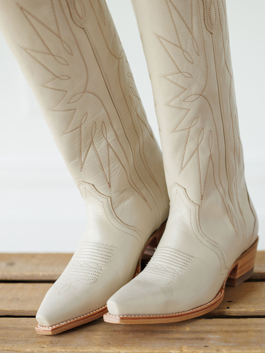 The Loretta Boot {Cream} by Savannah Sevens western life{&}style: tall, light beige cowhide leather Western boots with decorative stitching and pointed toes, displayed on a wooden surface. Boots handmade by Tecovas.