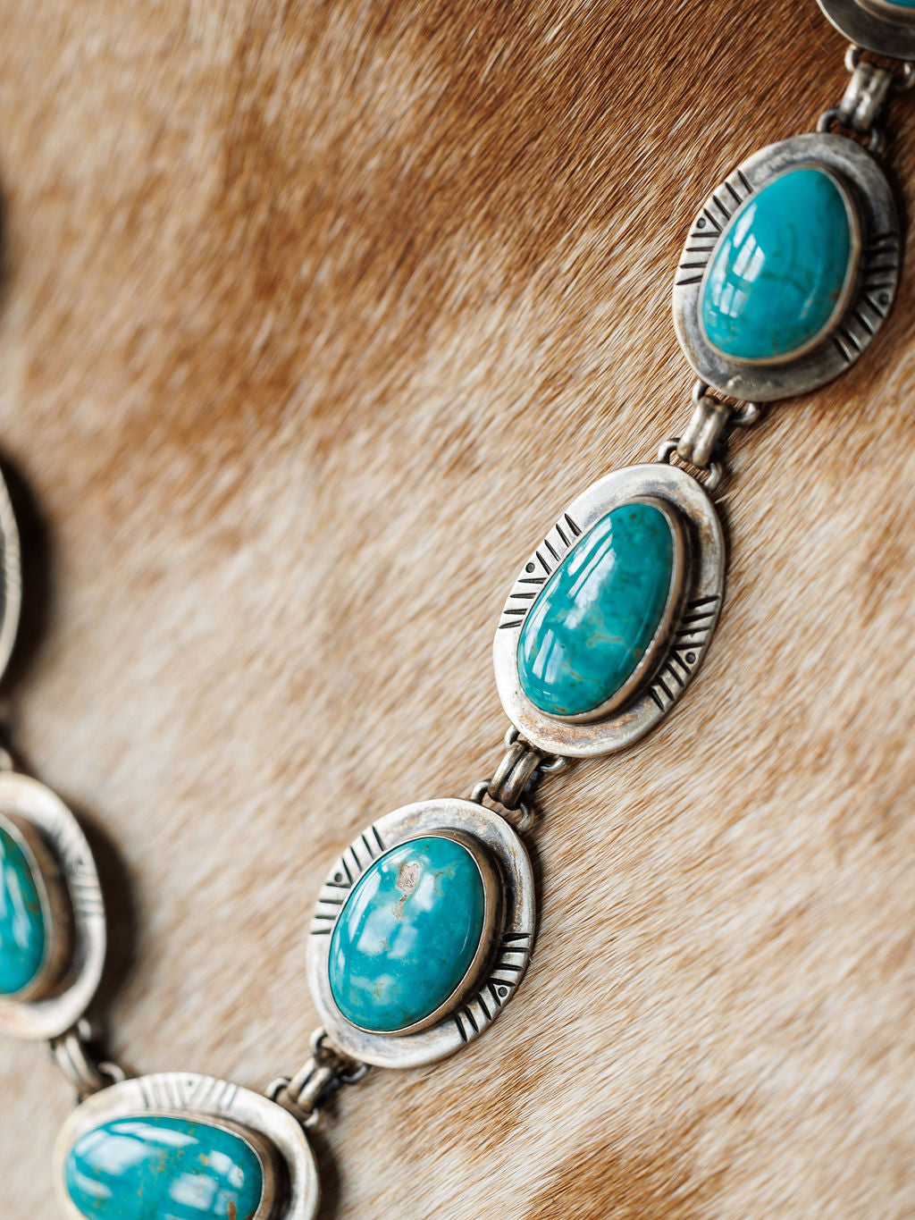 Close-up of the Nogales Necklace by Savannah Sevens western life{&}style, showcasing handmade oval Kingman turquoise stones set in engraved sterling silver on a light brown textured fur background.
