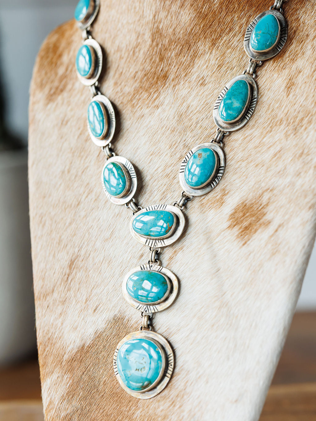 The Nogales Necklace by Savannah Sevens western life{&}style features large oval Kingman turquoise stones with intricate metalwork, displayed on a tan and white cowhide bust.
