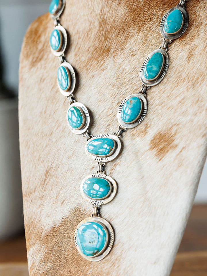 The Nogales Necklace by Savannah Sevens western life{&}style features large oval Kingman turquoise stones with intricate metalwork, displayed on a tan and white cowhide bust.