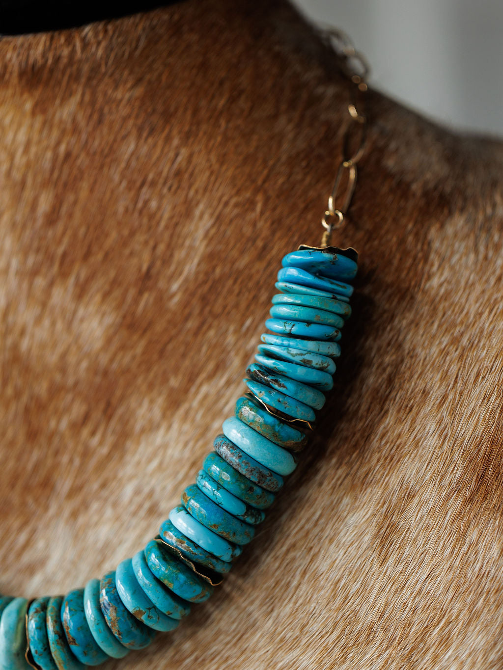 A Kingman Necklace by Savannah Sevens western life{&}style, featuring round, flat turquoise stones, is shown worn on a cowhide bust.