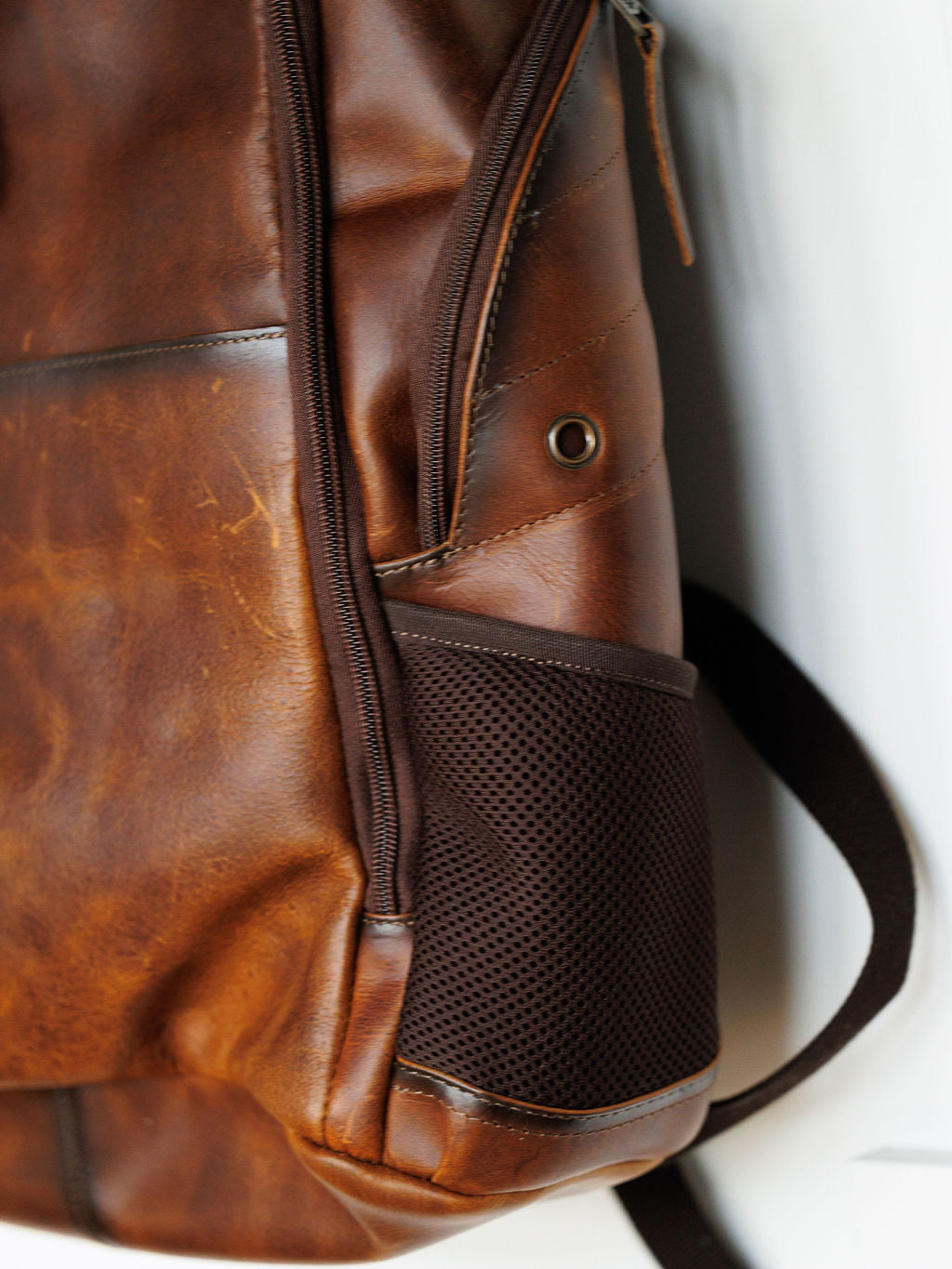 Close-up of the Waynesboro Backpack by Savannah Sevens western life{&}style, showing its full grain leather with natural creases, a visible zipper, metal rivet, and black mesh side pocket—details that highlight its quality and character.