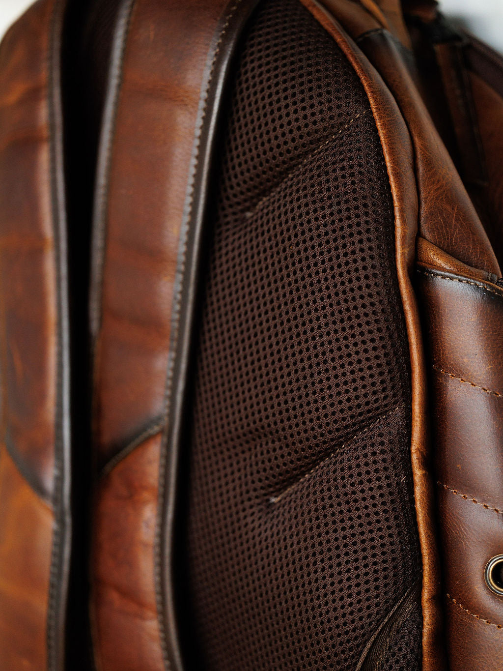 Close-up of the Waynesboro Backpack by Savannah Sevens western life{&}style, focusing on the padded black breathable mesh back panel and straps, with detailed stitching and texture of brown full grain leather.