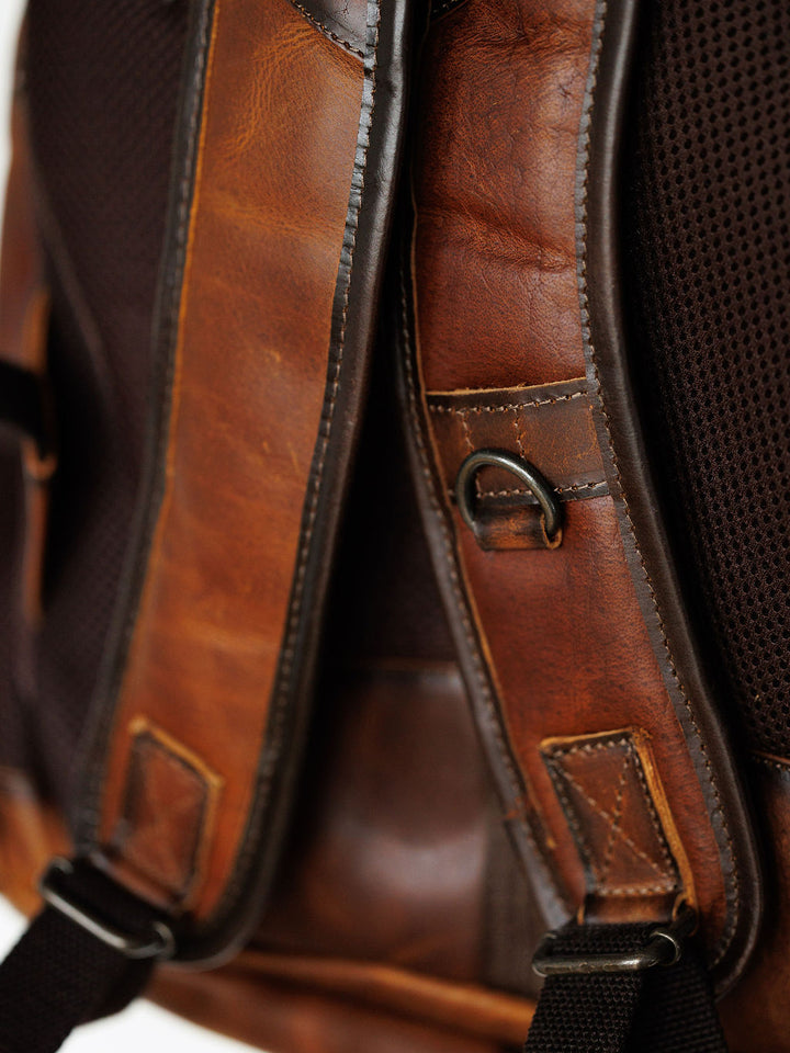 Close-up of the Waynesboro Backpack by Savannah Sevens western life{&}style, showing a full grain leather strap with detailed stitching, a metal D-ring, and black mesh padding in the background.