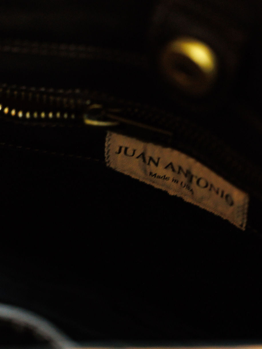 Close-up of a fabric label inside The Nubuck dark nubuck leather handbag by Savannah Sevens western life{&}style, reading "Made in USA," with a nearby zipper and brass button.