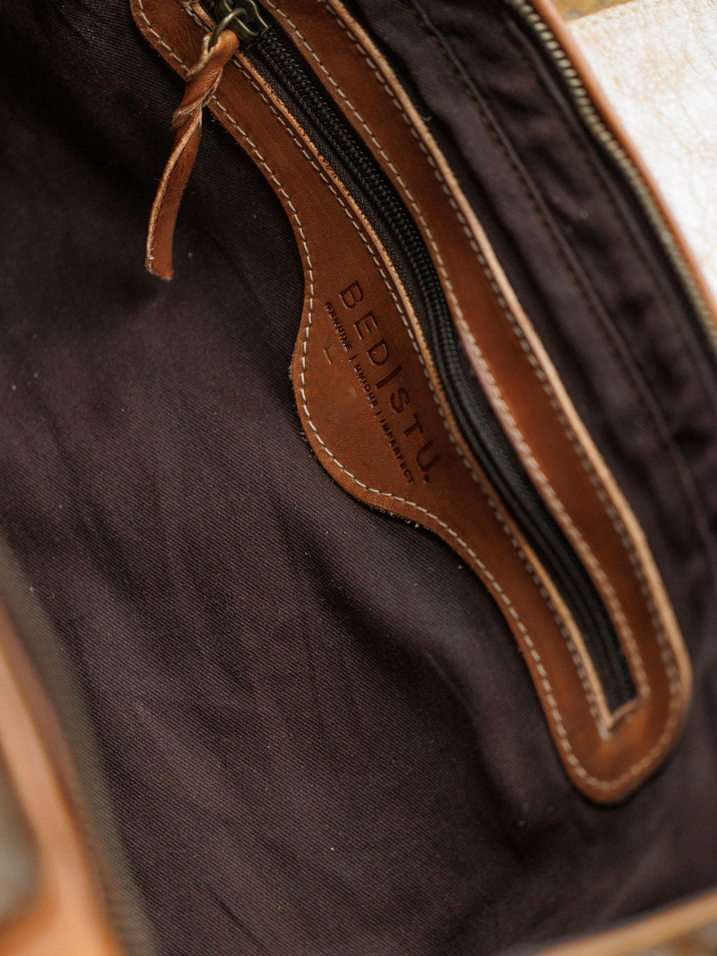 Close-up of The Rowley by Savannah Sevens western life{&}style, showing rustic leather trim, black fabric lining, and a zippered pocket embossed with the brand name inside.