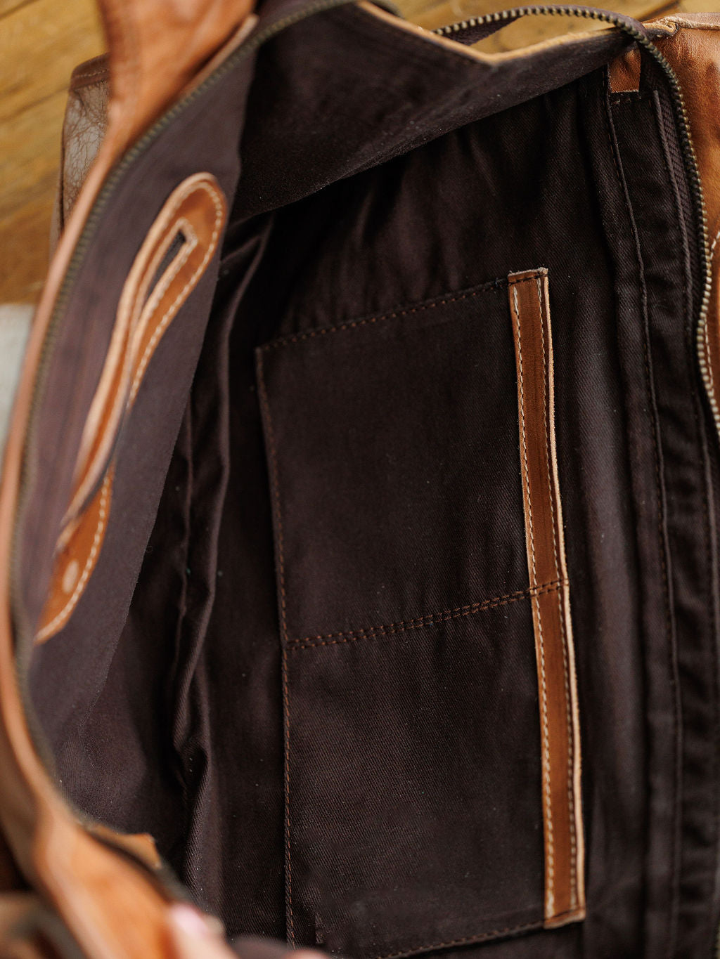 The Rowley by Savannah Sevens western life{&}style is a rustic full grain leather handbag featuring a dark fabric lining, two stitched pockets, and a leather-edged zipper compartment; the image shows its detailed interior.