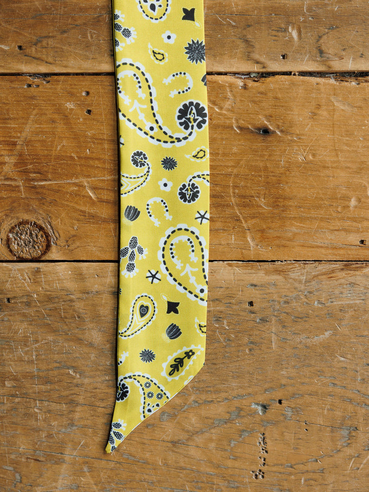 The Lucky Paisley Twilly {Yellow} by Savannah Sevens western life{&}style, featuring a black and white paisley print, rests on a rustic wooden surface.