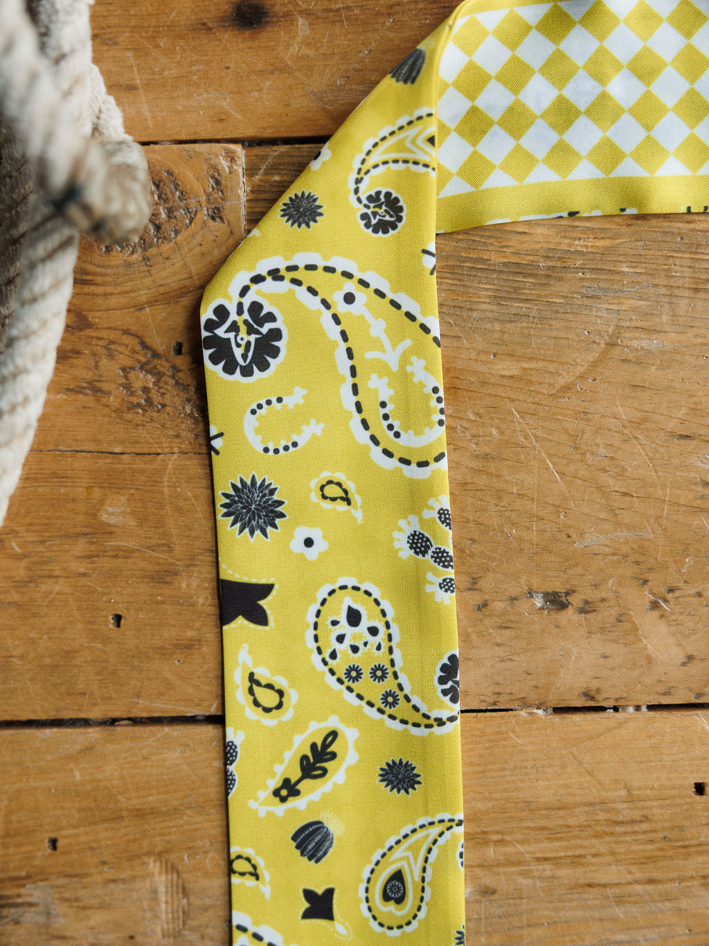 The Lucky Paisley Twilly {Yellow} by Savannah Sevens western life{&}style features a yellow chiffon scarf with paisley print and floral pattern, a yellow and white diamond check in the top corner, all set on rustic wood beside a thick rope.