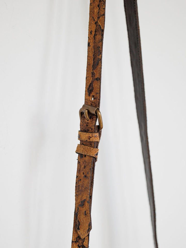 A close-up of The Nubuck by Savannah Sevens western life{&}style—a brown nubuck leather strap with metal hardware and subtle wear, set against a plain light background.
