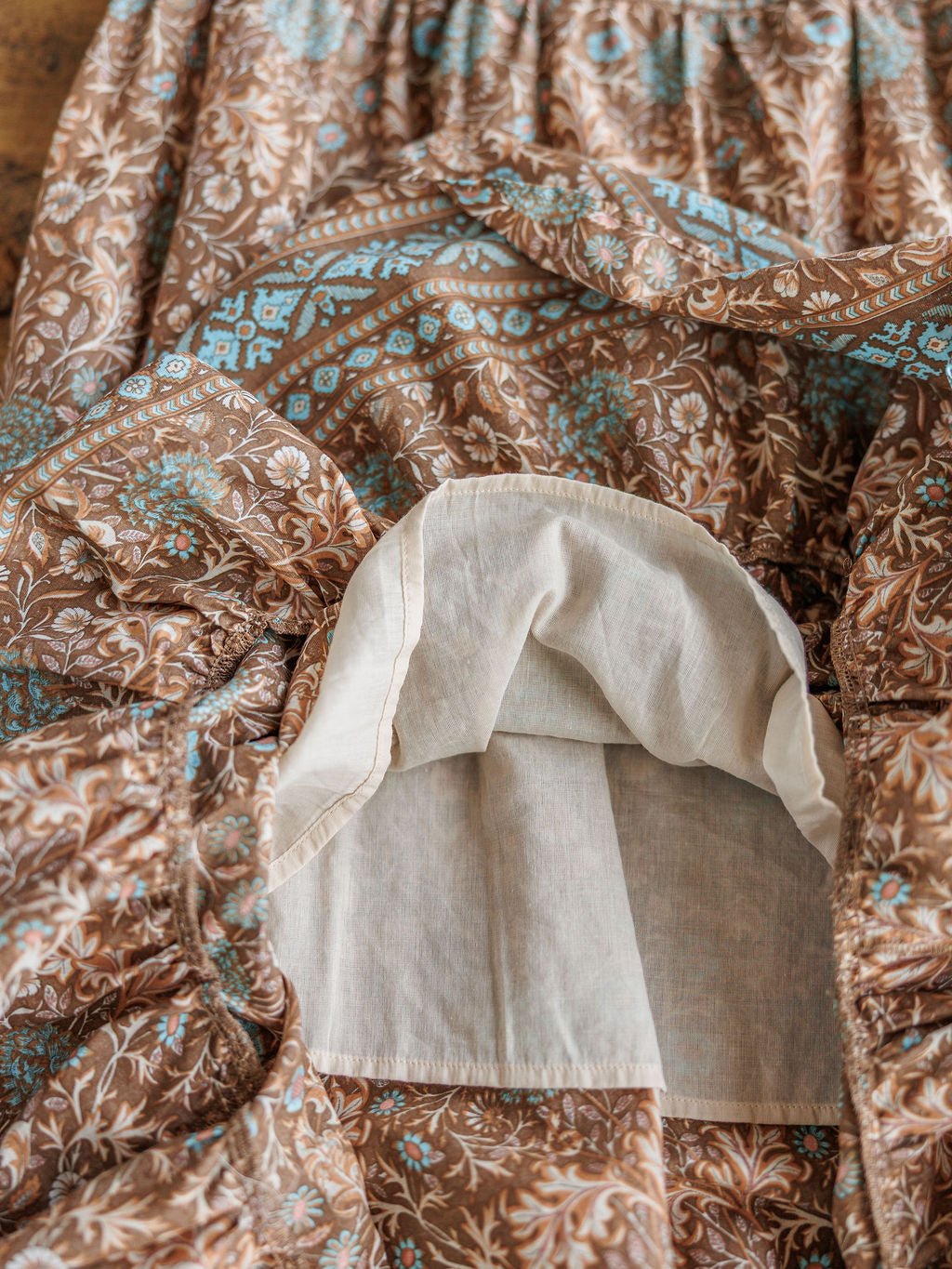 A close-up of The Mayetta dress by Savannah Sevens western life{&}style highlights its brown and blue floral patterns with exposed white cotton pocket lining, showcasing detailed fabric and inner construction.