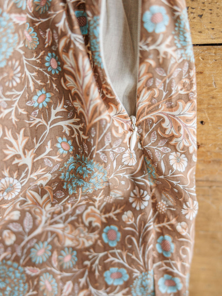 Close-up of The Mayetta dress by Savannah Sevens western life{&}style, showing beige, blue, and white floral fabric with a partially open zipper near the seam, laid on a wooden surface.