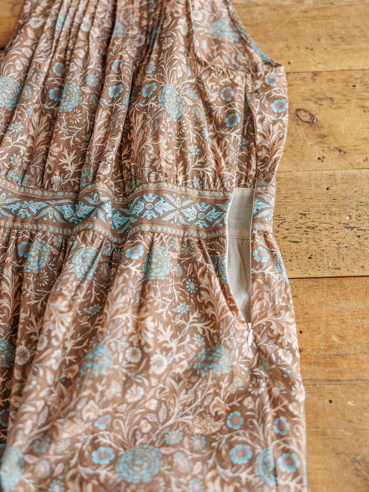 A close-up of The Mayetta dress by Savannah Sevens western life{&}style showcases blue and white floral designs, a geometric waistband, and a visible side pocket, all laid flat on a wooden surface.