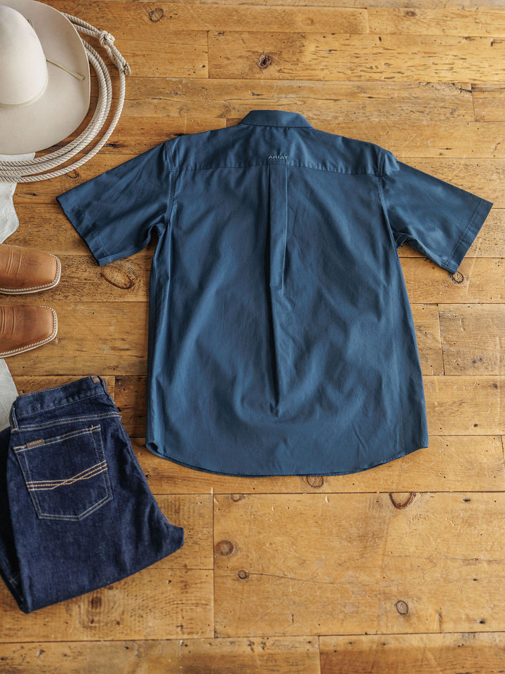 The Wellman men's short sleeve button up shirt by Savannah Sevens western life{&}style is laid flat with a beige cowboy hat, brown boots, and dark blue jeans for a timeless, classic Western look.