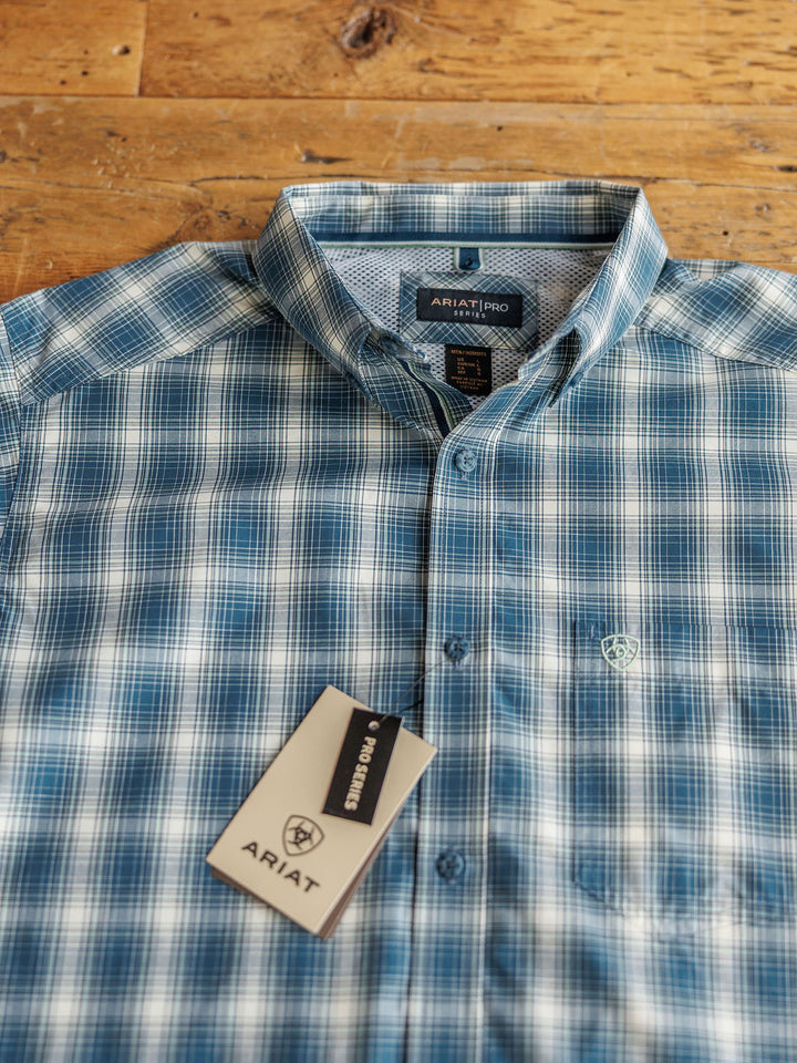 A blue and white plaid long sleeve shirt, "The Davis {Men's}" by Savannah Sevens western life{&}style, is neatly folded on a wooden surface with the brand logo on the chest and a branded tag attached.