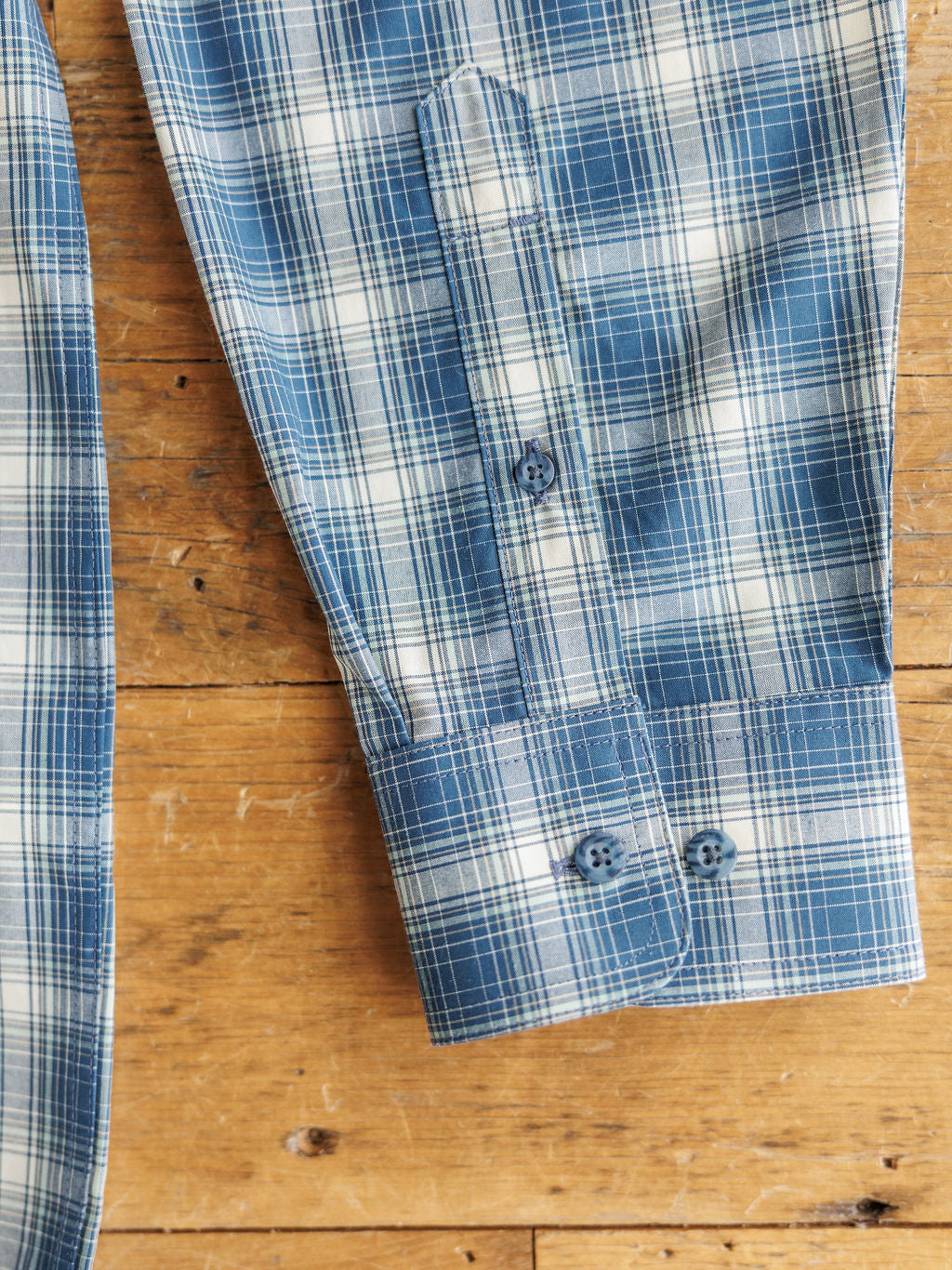 A close-up of The Davis Men's blue and white plaid long sleeve shirt by Savannah Sevens western life&style, featuring a cuff with two buttons. Fabric provides sun protection and moisture wicking for comfort.