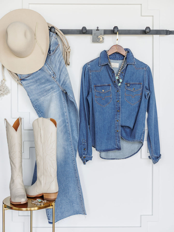 The Dalles by Savannah Sevens western life{&}style—a light tan cowboy hat, relaxed fit jeans, western yoke denim shirt, and white cowboy boots—are arranged against a white wall; jeans and shirt hang on hooks, boots rest on a round gold table.