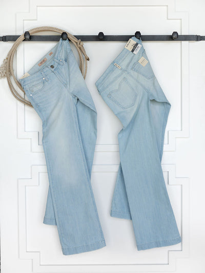 Two pairs of The Dani Perfect Rise Trouser Jean *Exclusive* by Savannah Sevens western life{&}style hang on a black rod against a white wall, with a coiled rope also hanging on the left side.