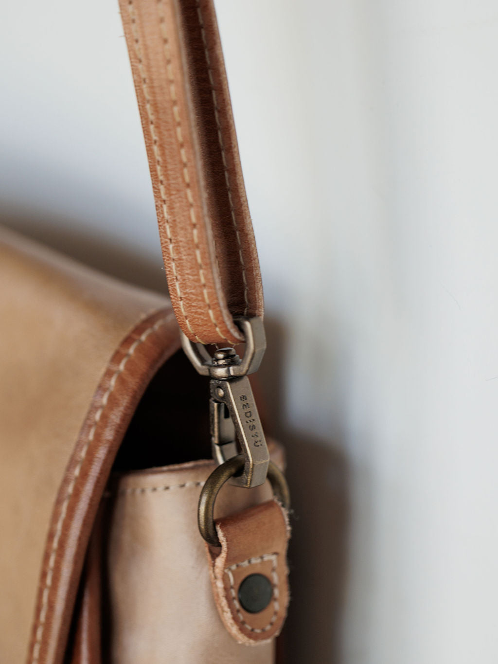 Close-up of The Lomita crossbody bag by Savannah Sevens western life{&}style, showcasing rustic oat leather, a metal clasp on the strap, visible stitching, and a small black rivet.