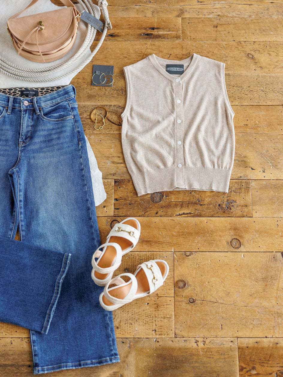The Moran: a casual outfit by Savannah Sevens western life{&}style—blue jeans, beige sleeveless button-up top, white sandals with gold buckles, beige handbag, gold hoop earrings, and a bangle styled on a wooden floor.