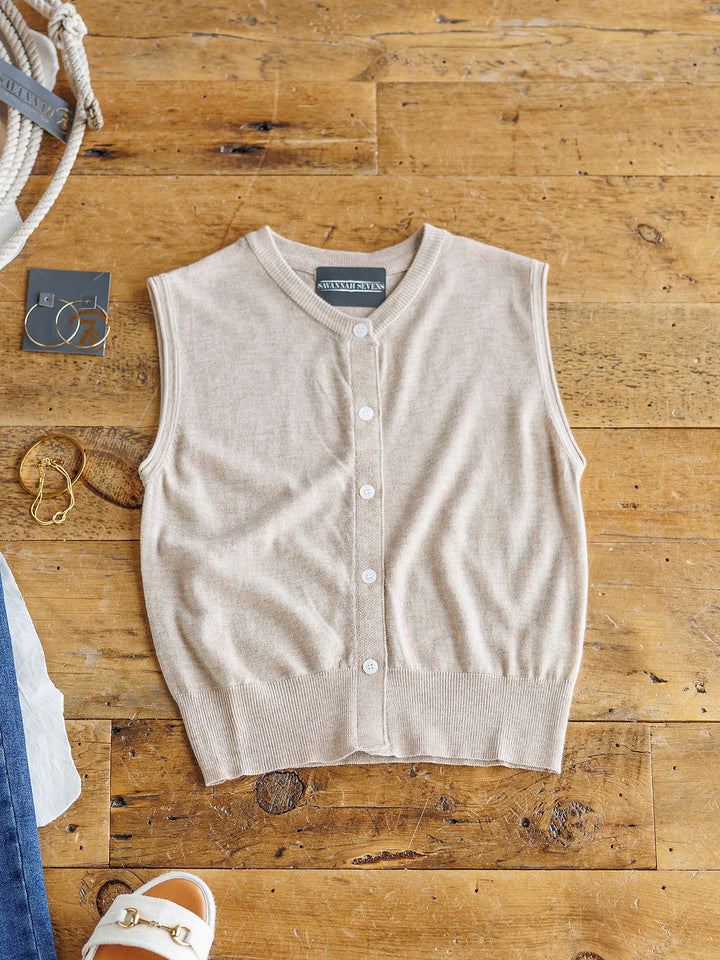 The Moran by Savannah Sevens western life{&}style is a beige wool blend, sleeveless button-up top with white buttons, shown laid flat on wood beside gold hoop earrings, bracelet, white sandals, and blue denim fabric.