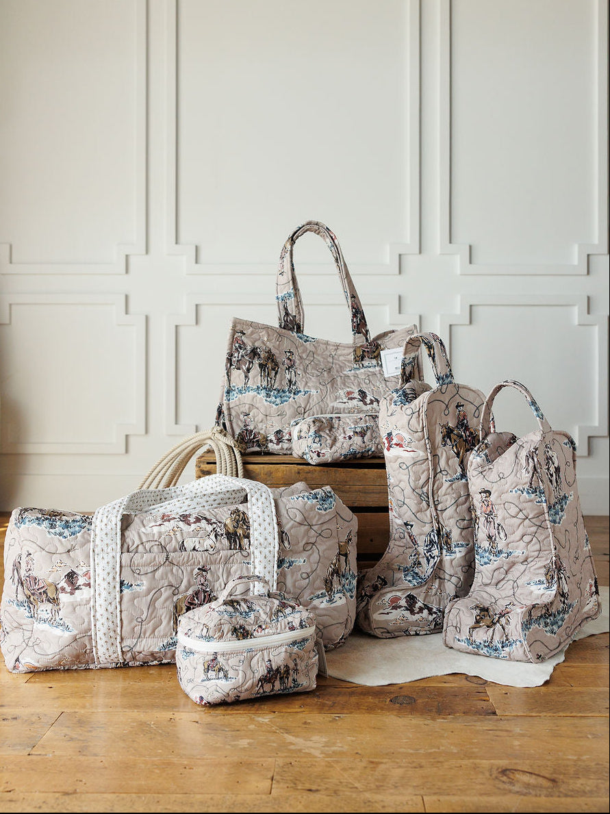 Five quilted travel bags and boots with a vintage map print from the Montana Summer Collection by Savannah Sevens western life&style are displayed on a wooden floor in front of a white paneled wall.