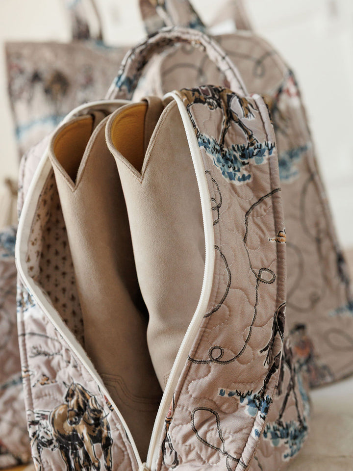 A close-up of a quilted bag set from the Montana Summer Collection by Savannah Sevens western life&style, showcasing a horse print and revealing beige cowboy boots inside. Similar patterned bags appear blurred in the background.